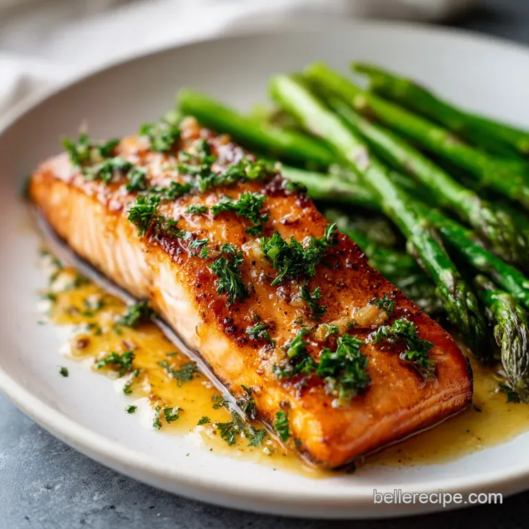 Flaky salmon fillet brushed with honey, next to bright green asparagus spears and a lemon wedge on a white plate.