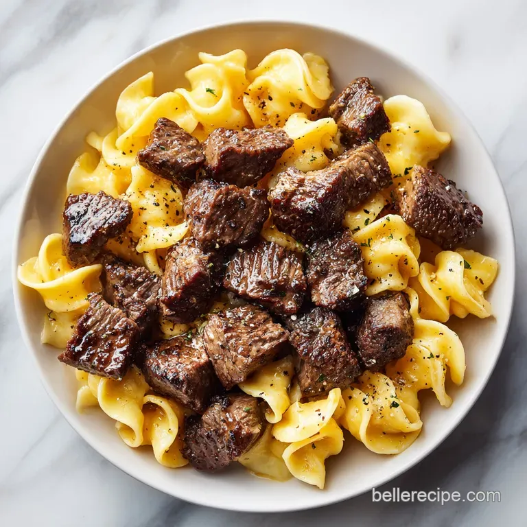 Tender beef chunks and golden wide noodles draped in a glossy sauce, served elegantly in a shallow modern bowl.
