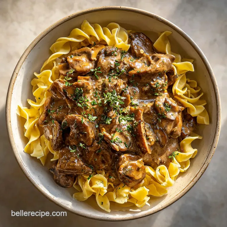 Elegant plate of beef stroganoff; glistening sauce coats the noodles, garnished with a dollop of sour cream and vibrant gr...