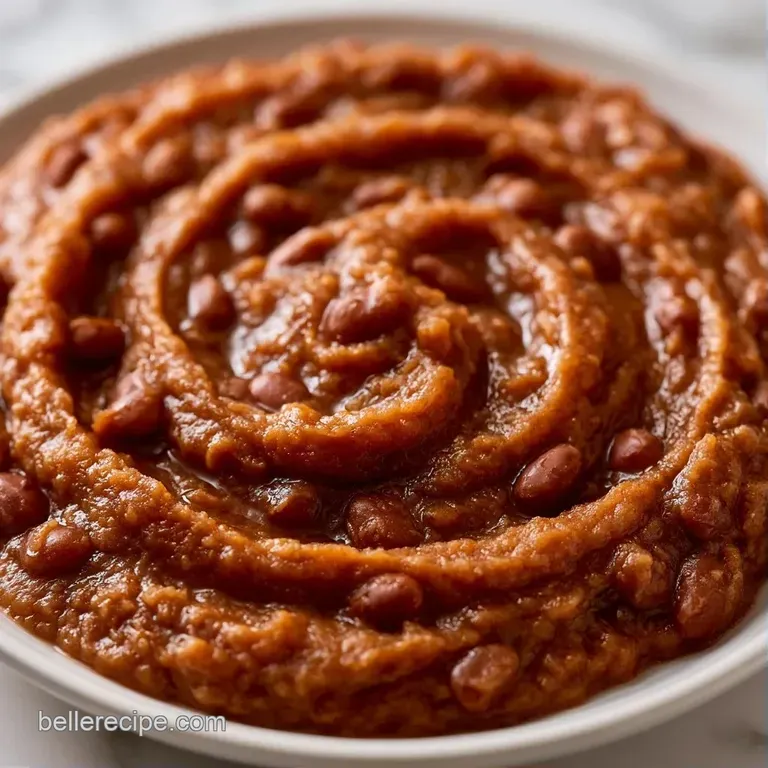 An elegant swirl of thick brown puree on a white plate, topped with bright red pickled onions and microgreens.