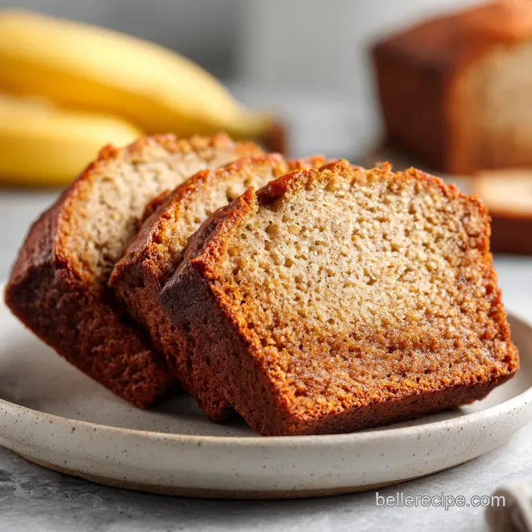 Elegant slice of banana bread on a white plate; visible moist crumb, powdered sugar dusting, and a vibrant strawberry garn...
