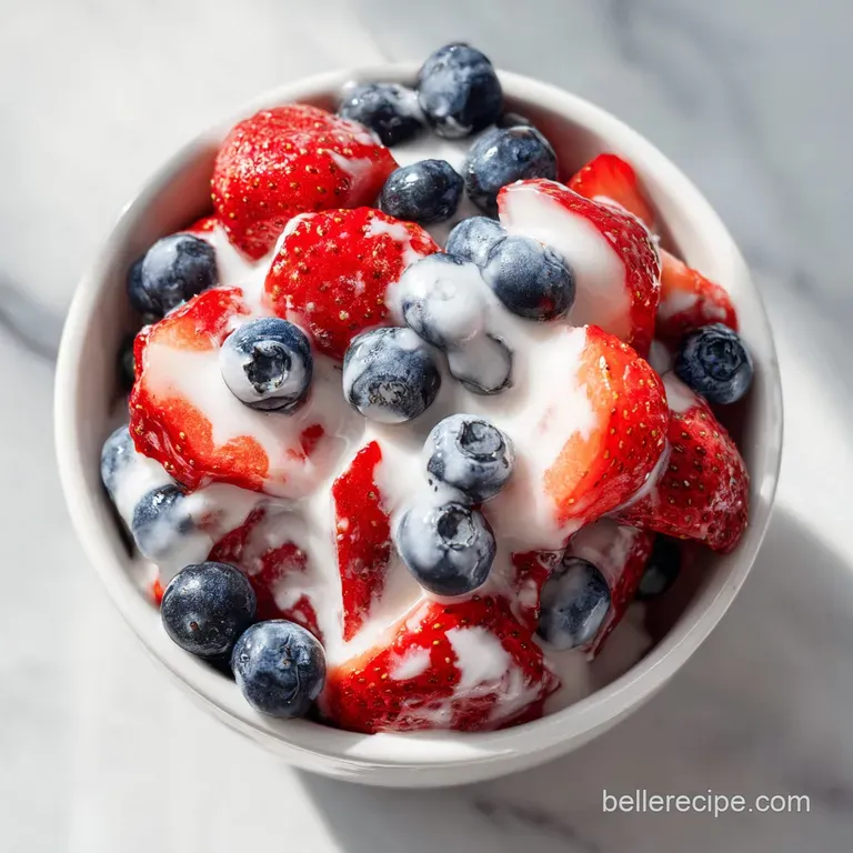 Fresh berries coated in a velvety white cream, served in a clear glass bowl topped with a sprig of green mint