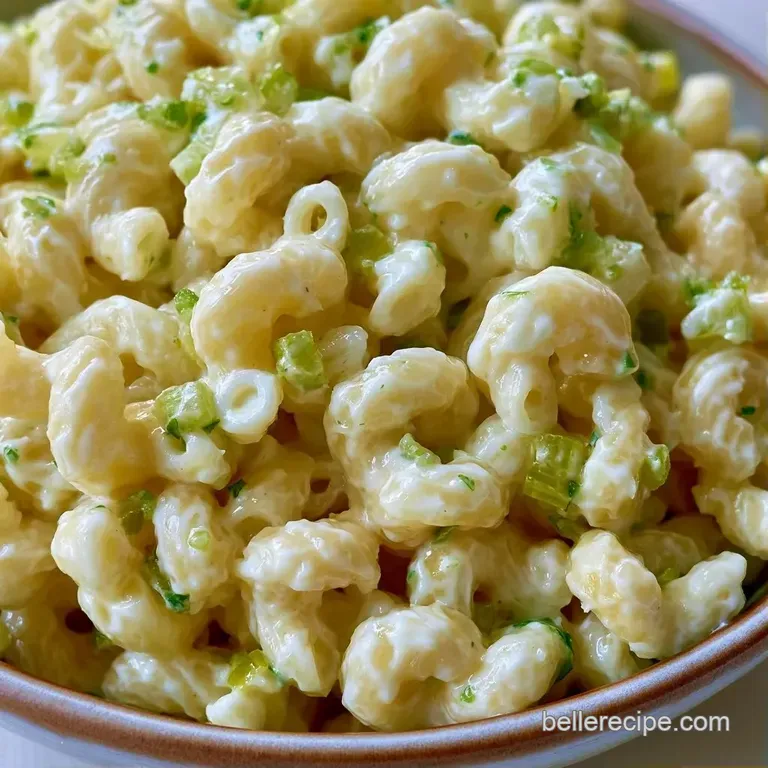 A chilled scoop of creamy pasta salad in a white dish, garnished with a pinch of red paprika and fresh green herbs.