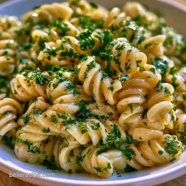 Vibrant pasta swirls mixed with chopped herbs and lemon zest, elegantly served on a matte grey minimalist plate.